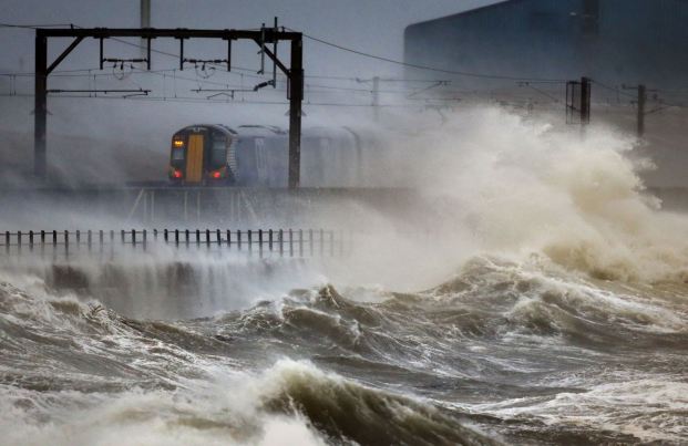 Waves crash against the railway embankment as a train edges along the coast at Saltcoats in Scotland. (PA)