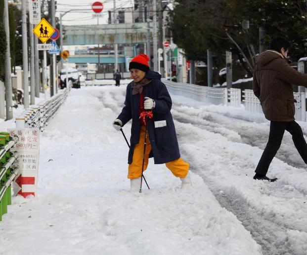 A woman crosses a snow-covered road assisted with walking sticks in Tokyo on February 9, 2014 (AFP Photo/Yoshikazu Tsuno)