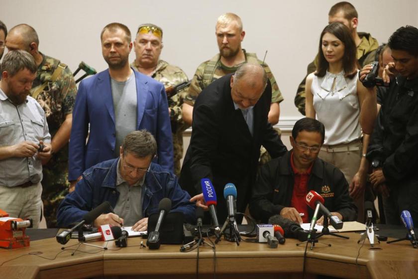 A representative (seated L) from pro-Russian separatists and Colonel Mohamed Sakri (seated R) of the Malaysian National Security Council sign documents after the handing over of Malaysia Airlines flight MH17's black boxes, in Donetsk July 22, 2014. The remains of some of the 298 victims of the Malaysia Airlines plane downed over Ukraine were making their way to the Netherlands on Tuesday as Senior Ukrainian separatist leader Aleksander Borodai (back L, in blue blazer) handed over the plane's black boxes to Malaysian experts. REUTERS/Maxim Zmeyev