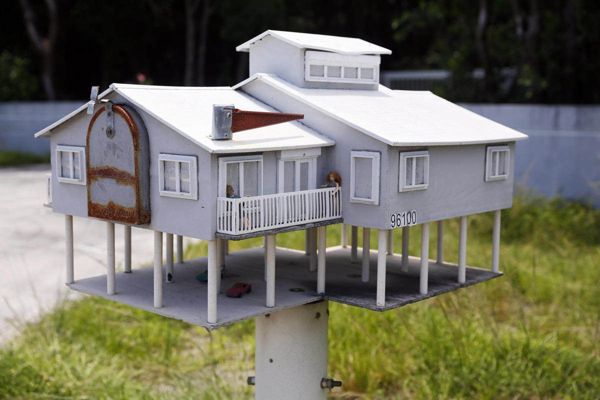 A mailbox in the shape of a house with a veranda and a parking lot is seen ...